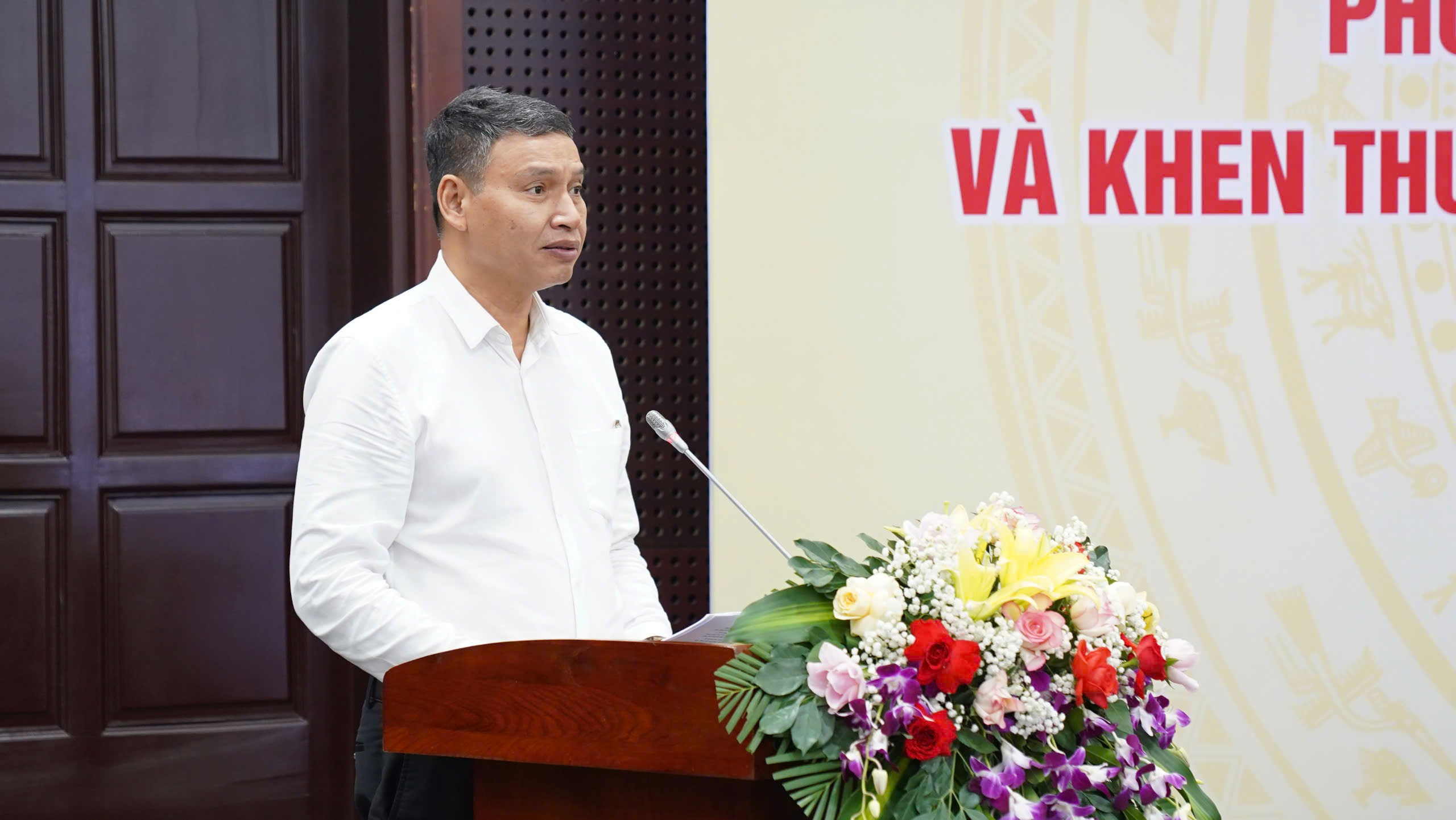 A person standing at a podium with a microphone and flowers

AI-generated content may be incorrect.